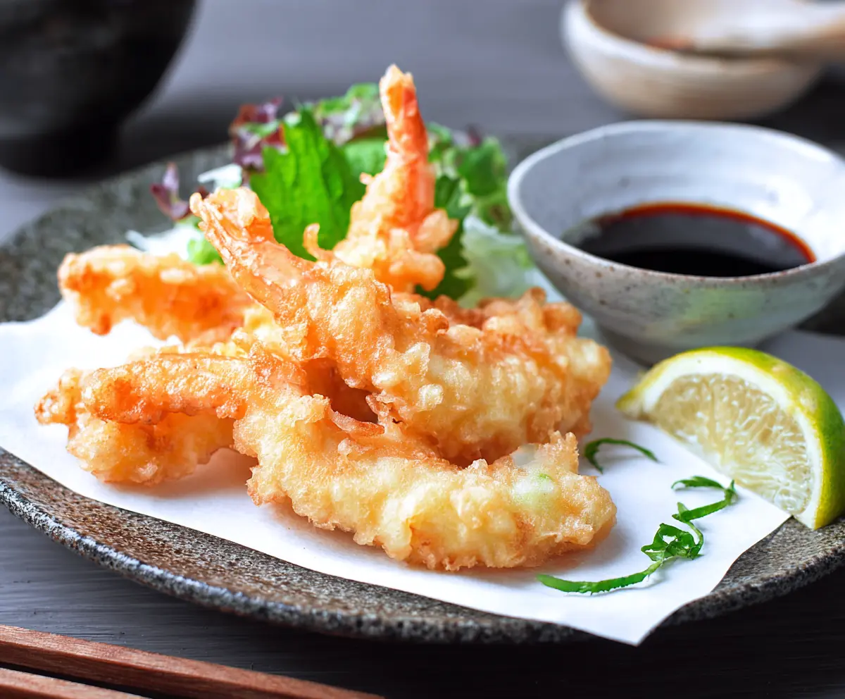 Crispy Japanese shrimp tempura served with dipping sauce on a traditional plate.