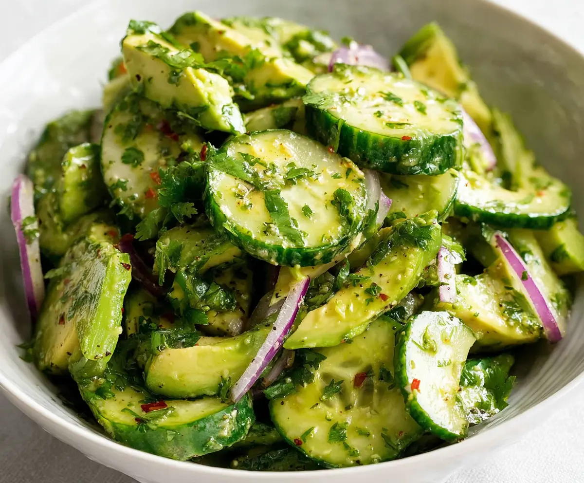 Fresh cucumber and ripe avocado salad with herbs on a white plate, healthy vegan appetizer.