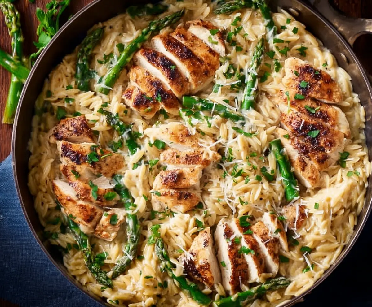 Creamy Parmesan orzo with grilled chicken and fresh asparagus on a white plate.