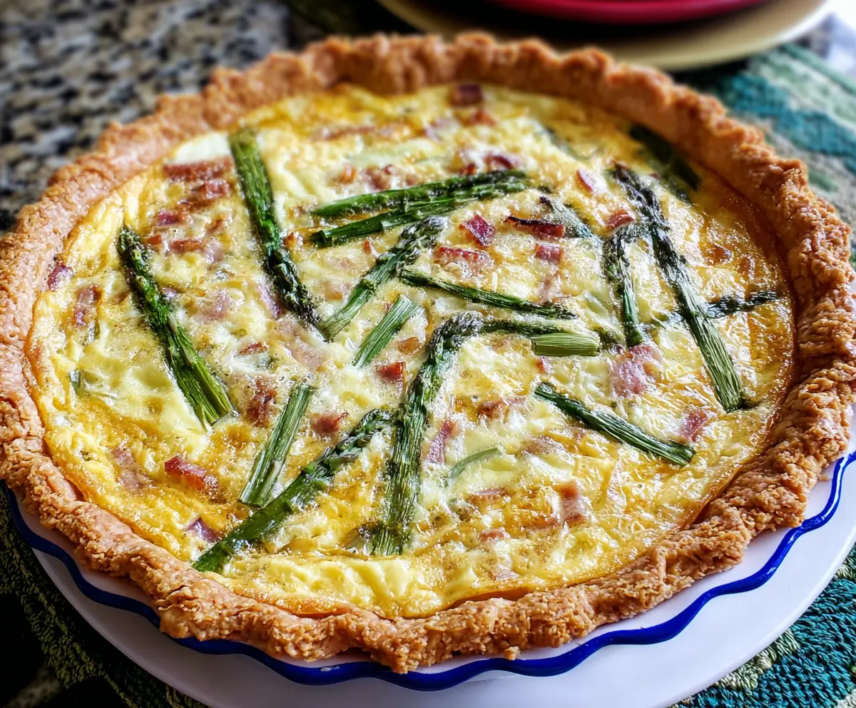 Delicious ham and asparagus quiche slice on a plate, garnished with herbs.
