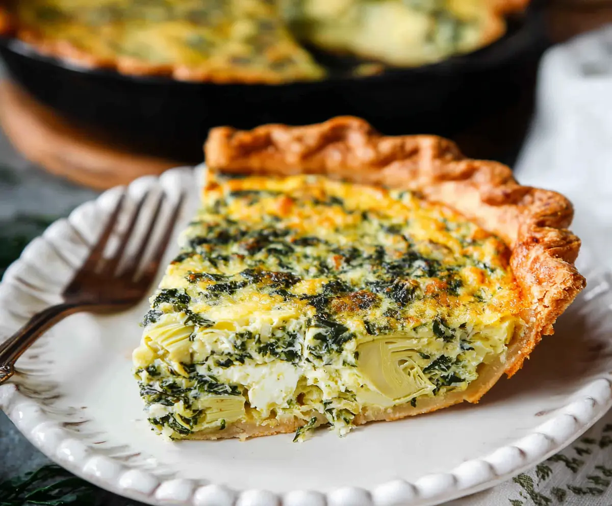 Delicious spinach and artichoke quiche with a golden crust on a plate.